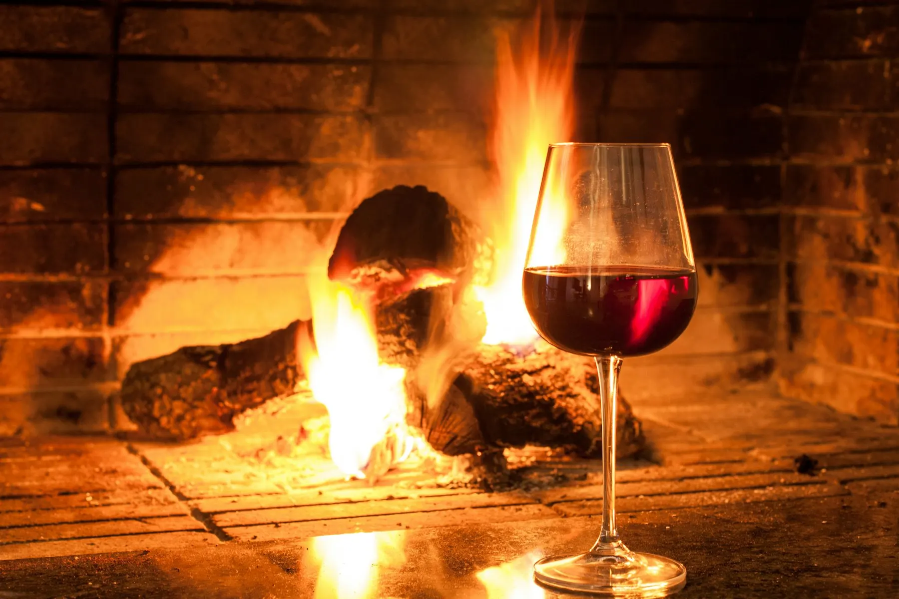 A glass of red wine in front of a glowing fireplace